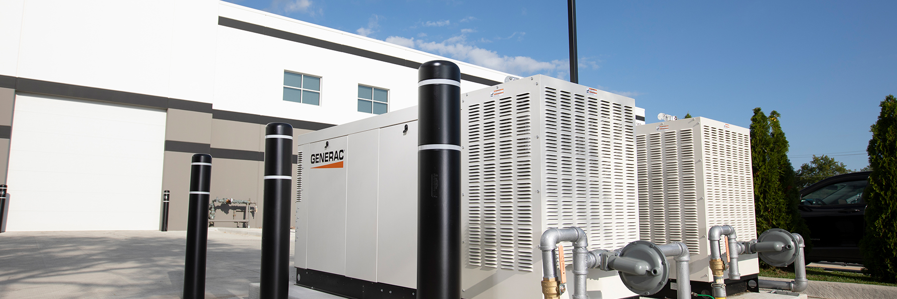 Industrial Generac standby generator with protective bollards installed outside commercial building, providing backup power for business operations