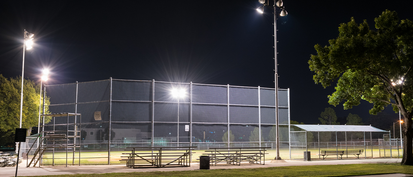 Outdoor athletic facility at night with professional sports lighting installation on tall poles illuminating tennis courts and bleachers commercial electrical service