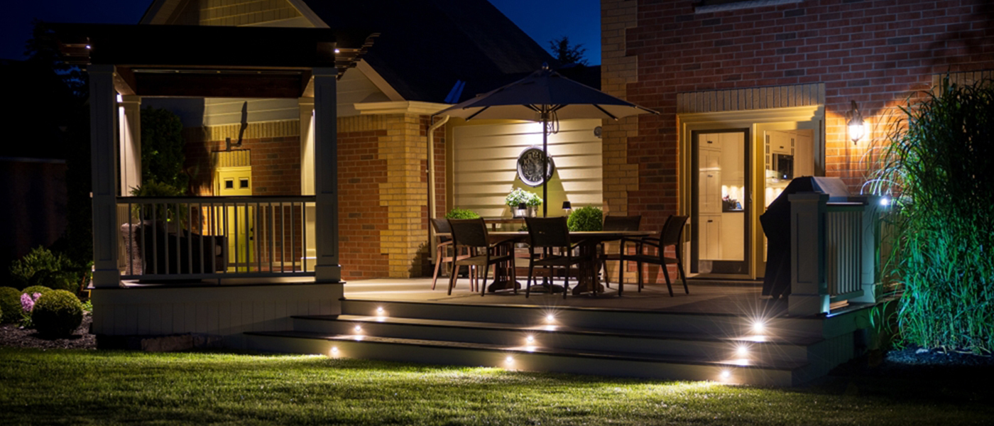 Residential outdoor deck at night with professional landscape lighting installation featuring LED step lights patio umbrella lighting and outdoor audio visual system outdoor electrical services