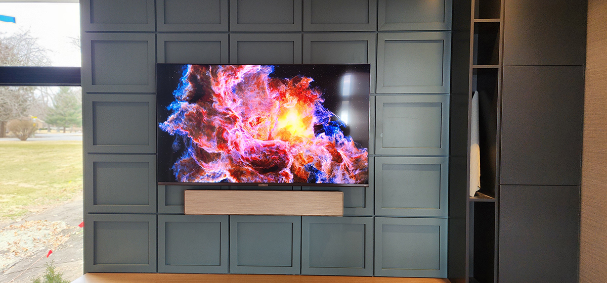 Large flat-screen TV mounted on custom dark gray paneled wall unit with integrated wooden soundbar in modern residential living room